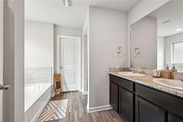 bathroom with a garden tub, wood finished floors, visible vents, and a sink