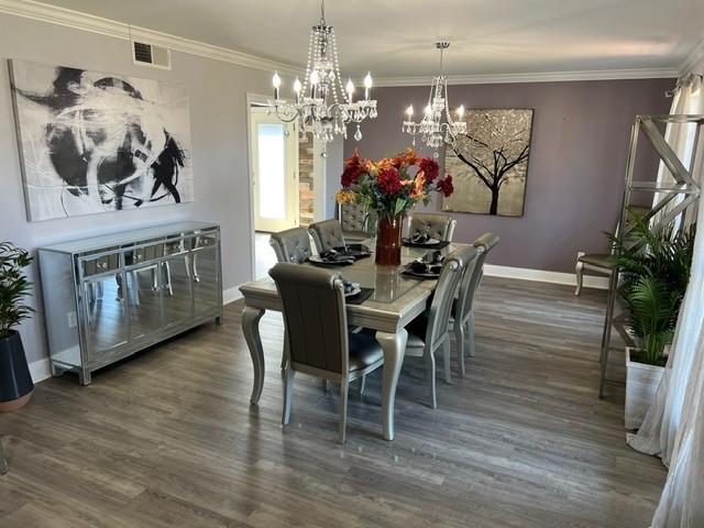 dining area featuring visible vents, dark wood-style floors, an inviting chandelier, crown molding, and baseboards