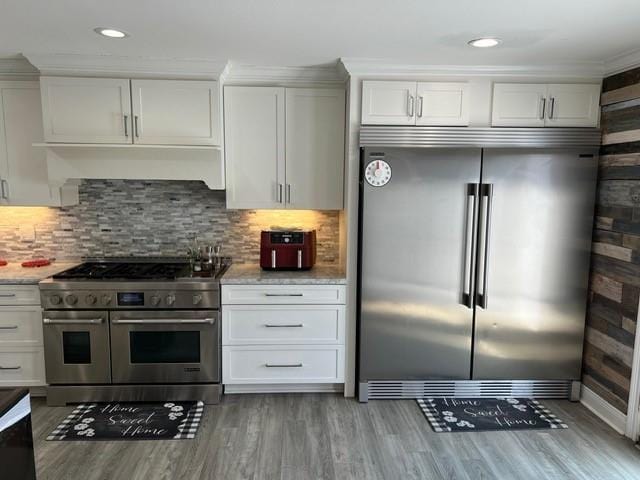 kitchen featuring backsplash, high quality appliances, white cabinets, and light wood finished floors