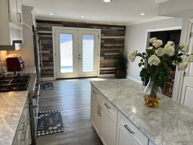 kitchen featuring light stone counters, french doors, white cabinets, crown molding, and dark wood-style flooring