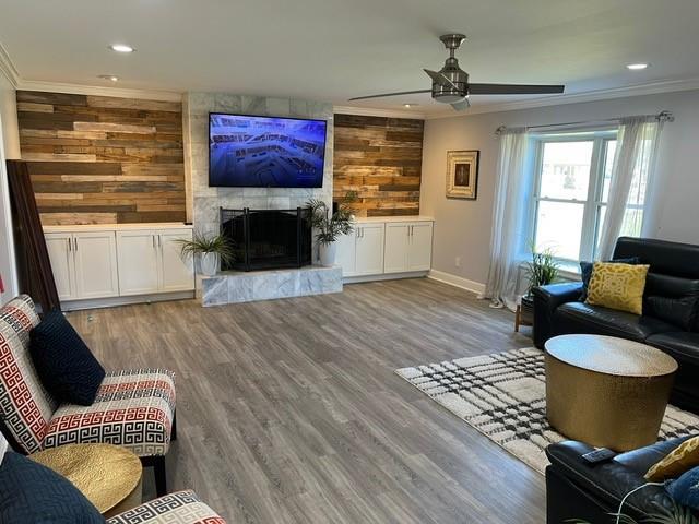 living area with a high end fireplace, wooden walls, crown molding, and wood finished floors