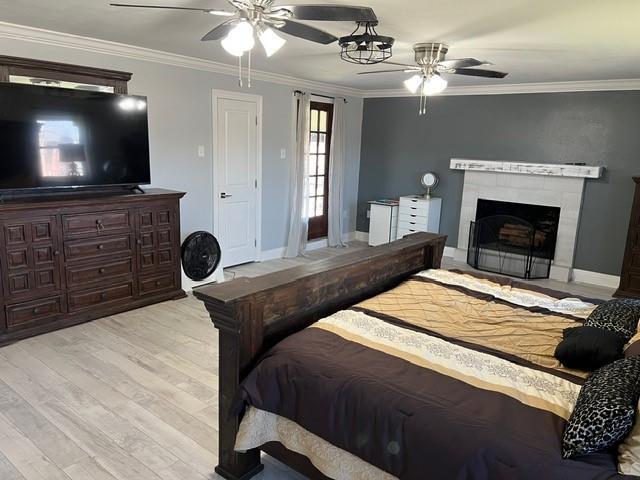 bedroom with a tiled fireplace, crown molding, wood finished floors, and a ceiling fan