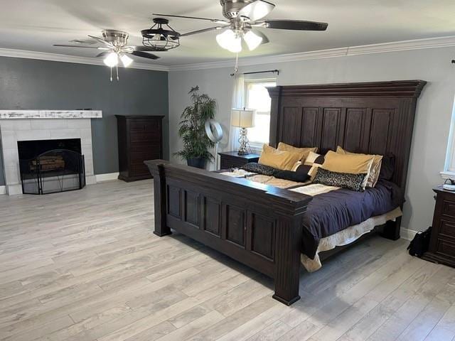 bedroom featuring a ceiling fan, light wood-style floors, ornamental molding, and a fireplace