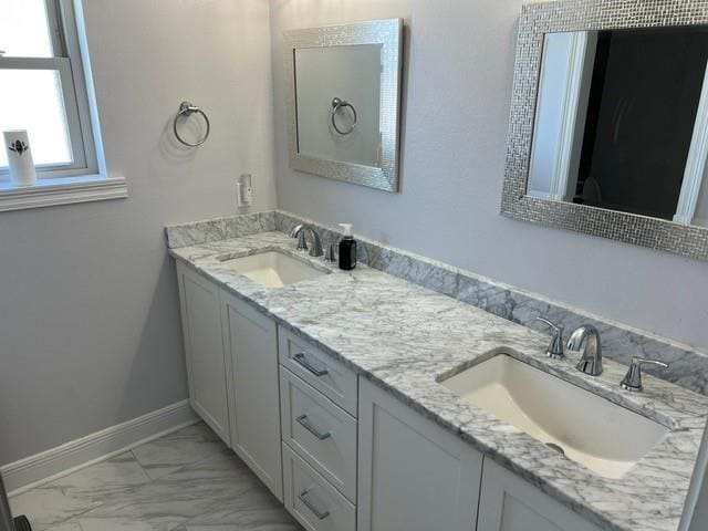 full bath with double vanity, marble finish floor, baseboards, and a sink