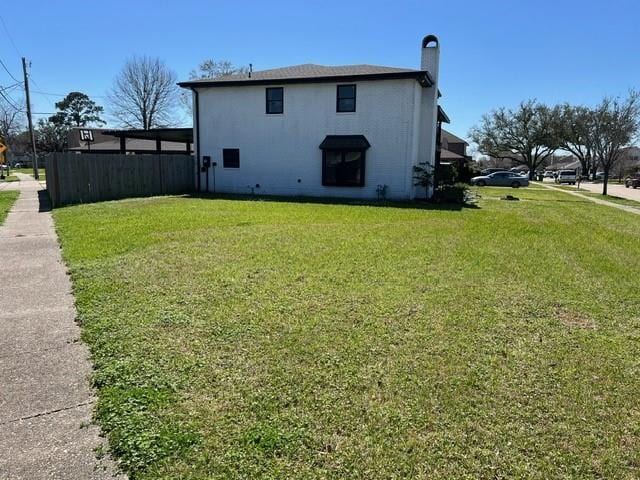 view of side of home featuring a lawn, a chimney, and fence