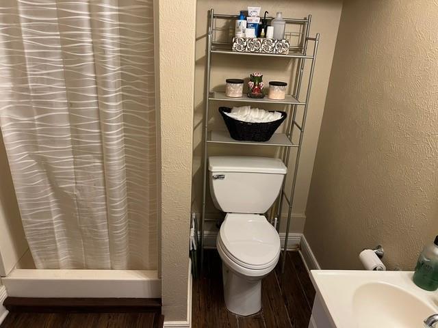 bathroom with a shower with curtain, wood finished floors, toilet, and a textured wall