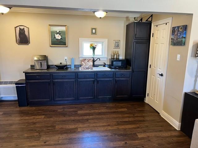 bar with dark wood-type flooring, a sink, black microwave, crown molding, and baseboards