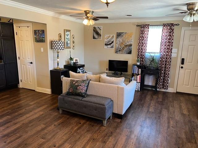 living area with dark wood finished floors, crown molding, and ceiling fan