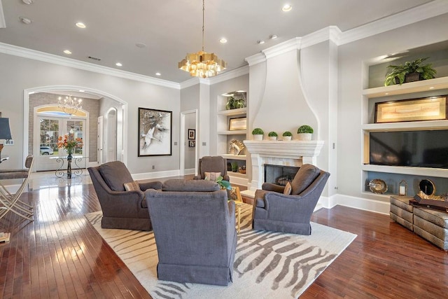 living area featuring a high end fireplace, built in features, an inviting chandelier, and hardwood / wood-style flooring