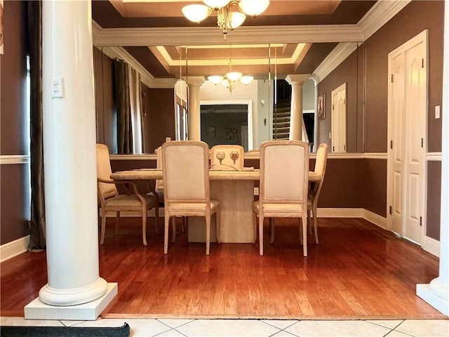 dining room featuring wood finished floors, ornate columns, crown molding, a raised ceiling, and a notable chandelier