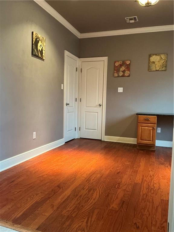 unfurnished room featuring visible vents, baseboards, dark wood-type flooring, and ornamental molding