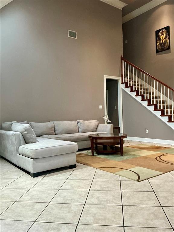 living area featuring light tile patterned floors, visible vents, baseboards, and stairway