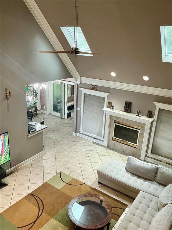 tiled living area with baseboards, ceiling fan, crown molding, and a tile fireplace