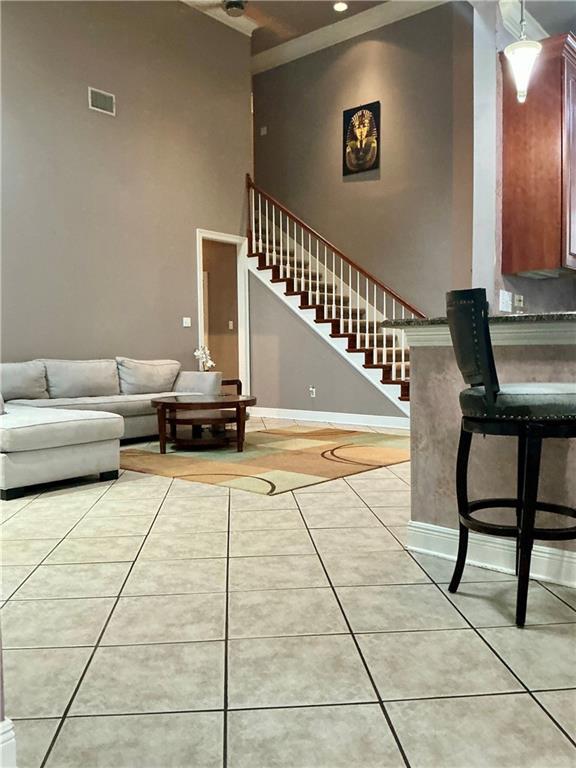 living area featuring visible vents, stairway, light tile patterned floors, baseboards, and a towering ceiling