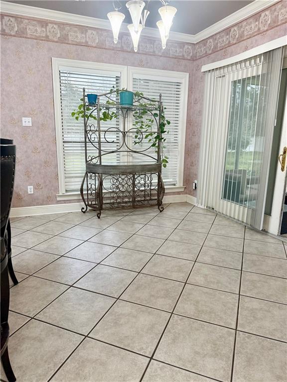 unfurnished dining area featuring light tile patterned floors, baseboards, crown molding, and an inviting chandelier