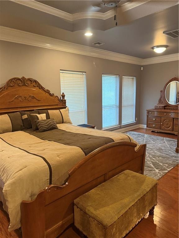 bedroom with visible vents, a tray ceiling, ornamental molding, a ceiling fan, and wood-type flooring