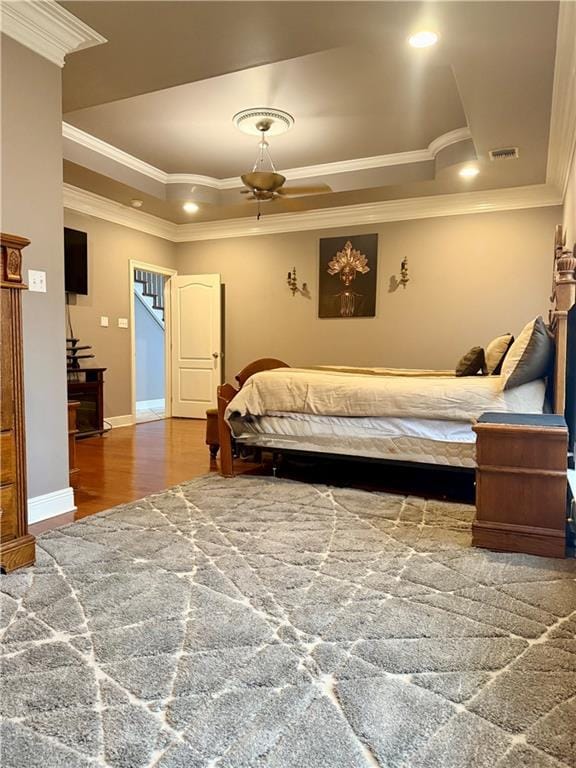 bedroom featuring visible vents, crown molding, a raised ceiling, and wood finished floors