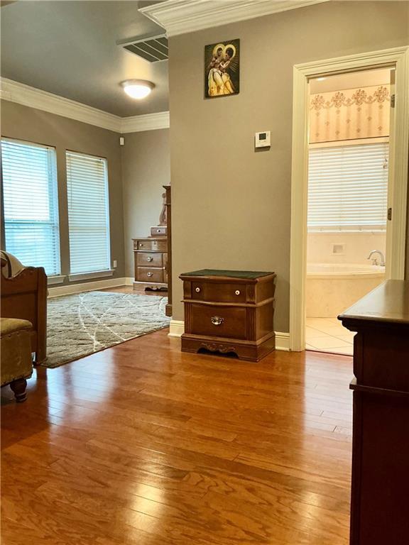 interior space with baseboards, wood finished floors, visible vents, and ornamental molding