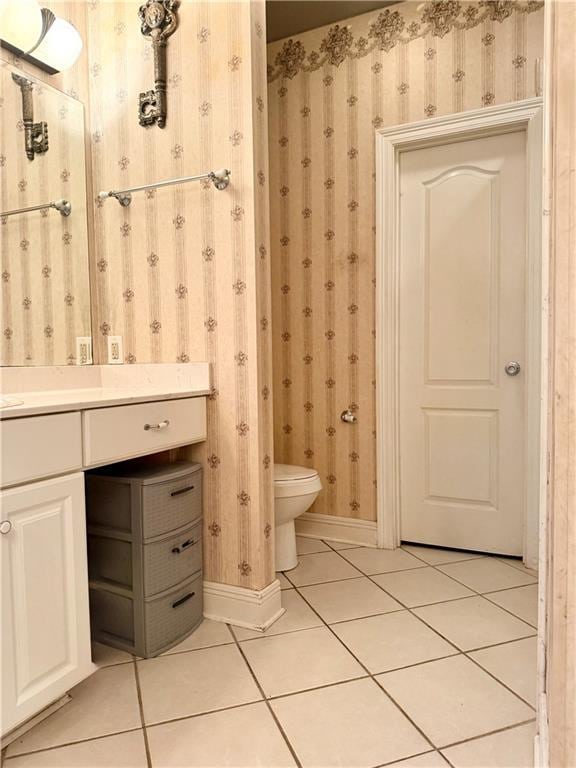 bathroom with tile patterned floors, toilet, wallpapered walls, baseboards, and vanity