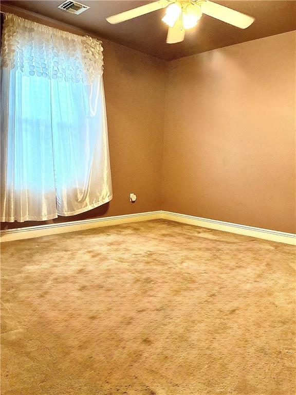 carpeted empty room featuring visible vents, baseboards, and ceiling fan