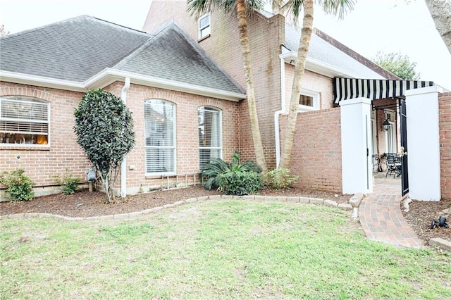 view of home's exterior featuring a yard, brick siding, and roof with shingles