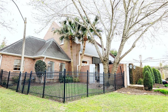 exterior space featuring brick siding, roof with shingles, a front yard, and fence