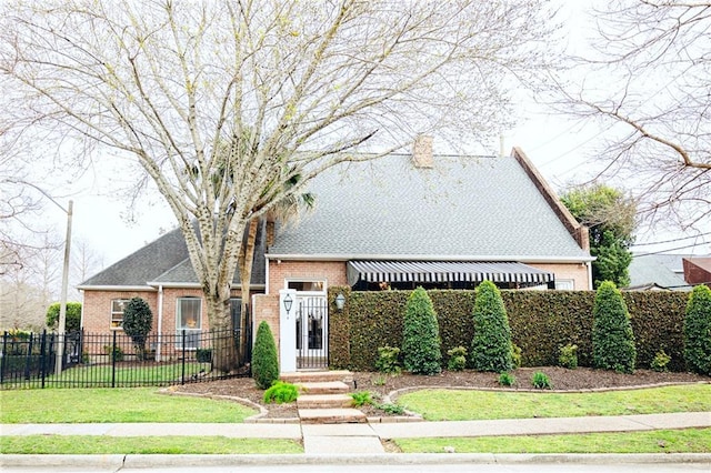 view of front of house featuring fence, roof with shingles, a front yard, brick siding, and a chimney