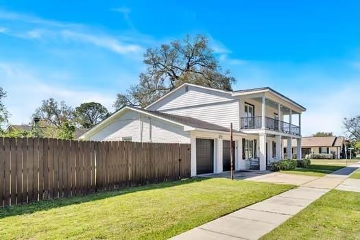 view of front facade with driveway, a front lawn, fence, an attached garage, and a balcony