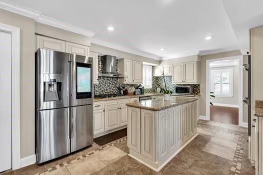 kitchen featuring a kitchen island, appliances with stainless steel finishes, crown molding, wall chimney range hood, and tasteful backsplash