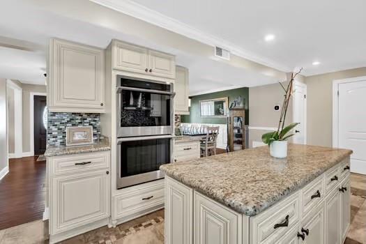 kitchen with light stone counters, a kitchen island, recessed lighting, decorative backsplash, and double oven