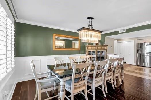 dining area featuring visible vents, a wainscoted wall, ornamental molding, wood finished floors, and a decorative wall