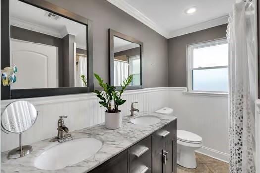 full bath with a sink, toilet, ornamental molding, and double vanity