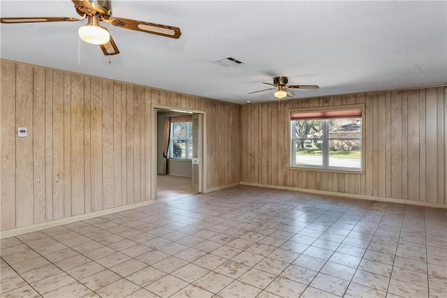 empty room featuring wooden walls, visible vents, baseboards, and ceiling fan