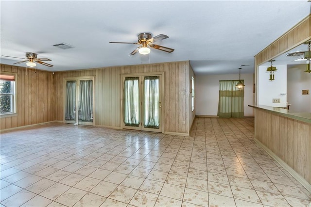 unfurnished room with wooden walls, visible vents, baseboards, and a ceiling fan