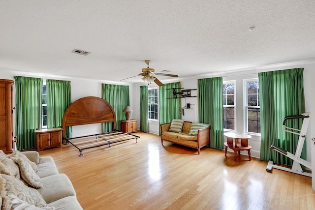 living area with visible vents, a textured ceiling, a ceiling fan, and wood finished floors
