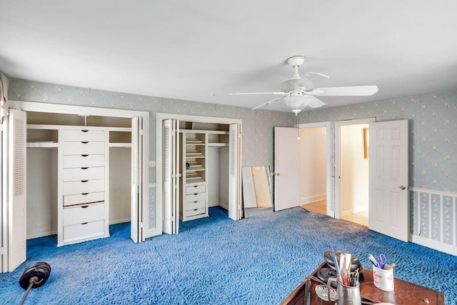 unfurnished bedroom featuring carpet flooring, wallpapered walls, multiple closets, and a ceiling fan