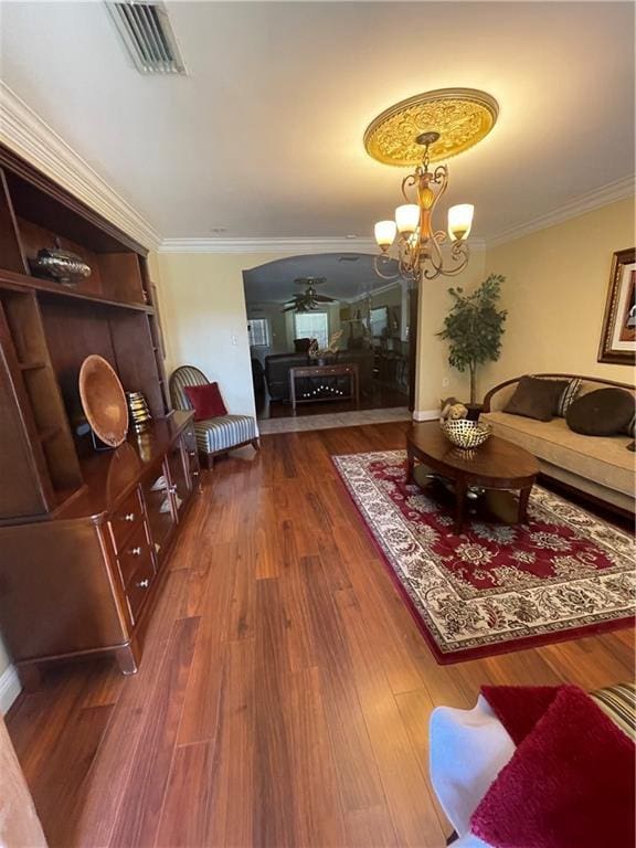 living area featuring visible vents, ceiling fan with notable chandelier, wood finished floors, arched walkways, and crown molding