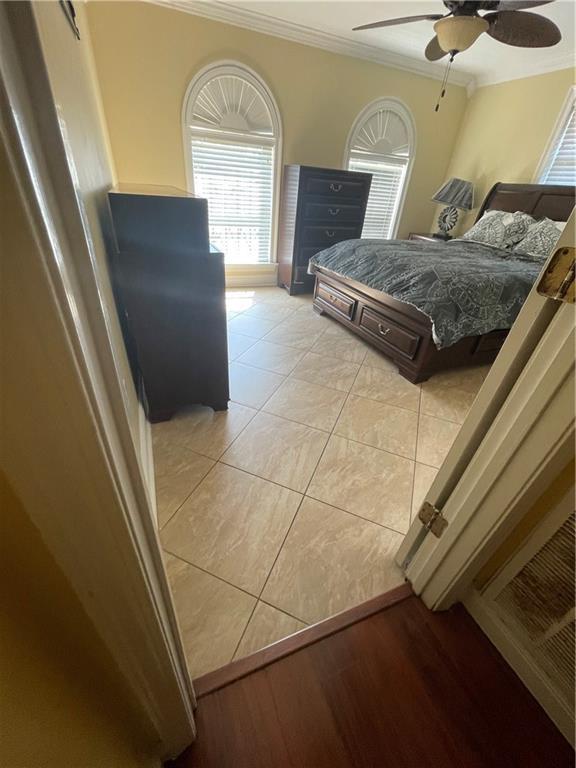 bedroom with crown molding, light tile patterned floors, and a ceiling fan