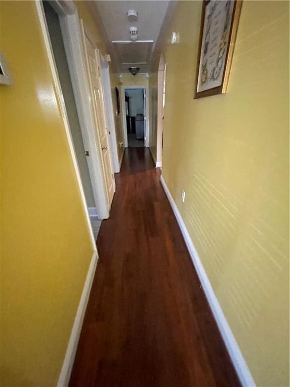 corridor featuring dark wood-type flooring, attic access, and baseboards