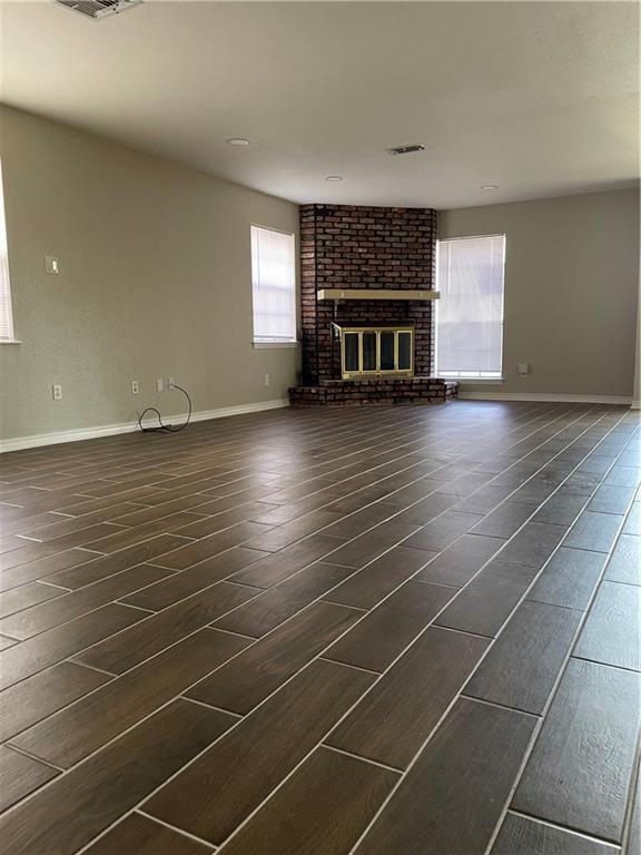 unfurnished living room with visible vents, a fireplace, dark wood-style flooring, and baseboards