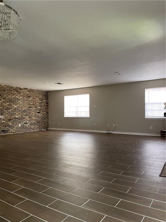 unfurnished room with baseboards, plenty of natural light, brick wall, and dark wood-style flooring