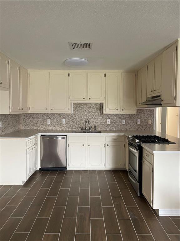 kitchen featuring visible vents, backsplash, under cabinet range hood, appliances with stainless steel finishes, and a sink