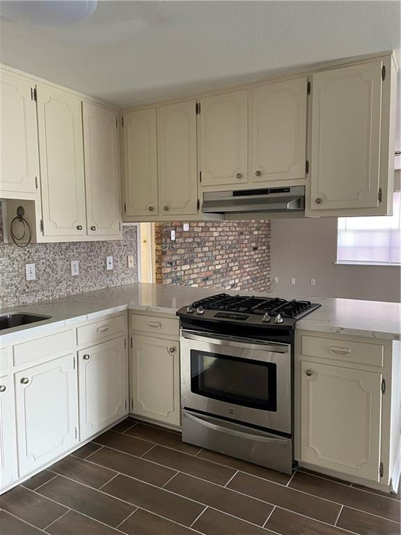 kitchen with gas stove, wood finish floors, light countertops, under cabinet range hood, and backsplash