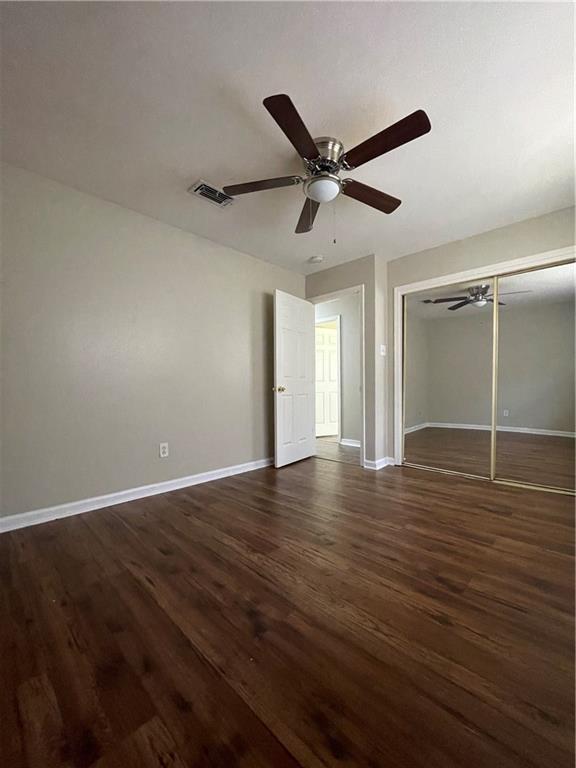 unfurnished bedroom with visible vents, dark wood-type flooring, a ceiling fan, a closet, and baseboards