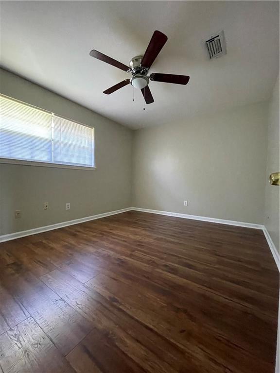 empty room with visible vents, ceiling fan, dark wood-type flooring, and baseboards