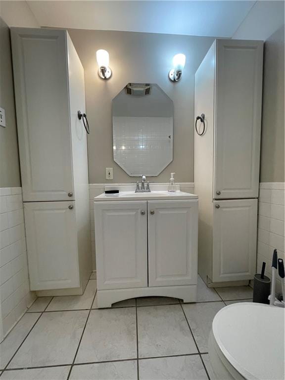 half bathroom featuring a wainscoted wall, toilet, tile walls, tile patterned flooring, and vanity