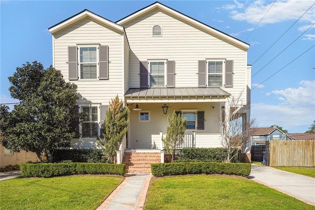 view of front of house featuring a standing seam roof, covered porch, a front yard, and fence