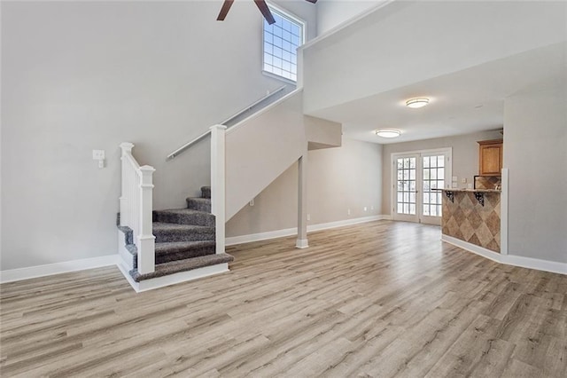 unfurnished living room with stairs, baseboards, light wood-type flooring, and french doors