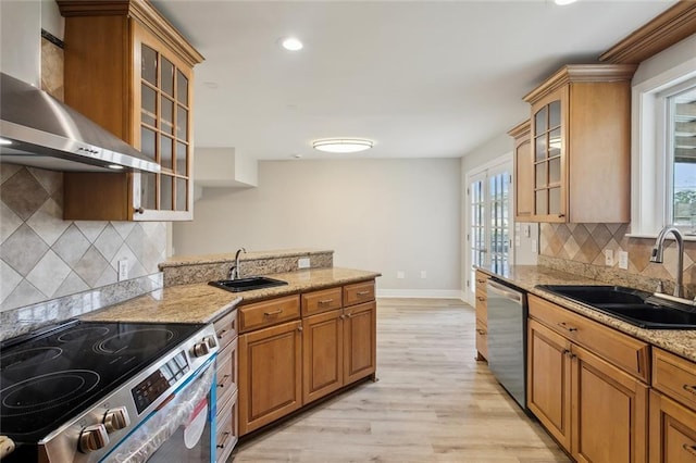 kitchen featuring wall chimney exhaust hood, light wood-style floors, appliances with stainless steel finishes, and a sink