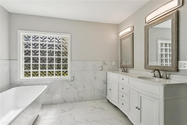 full bath with marble finish floor, a freestanding bath, tile walls, and a sink